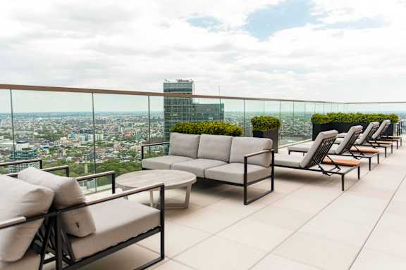 A patio with a couch, chairs, and a table overlooking a cityscape.