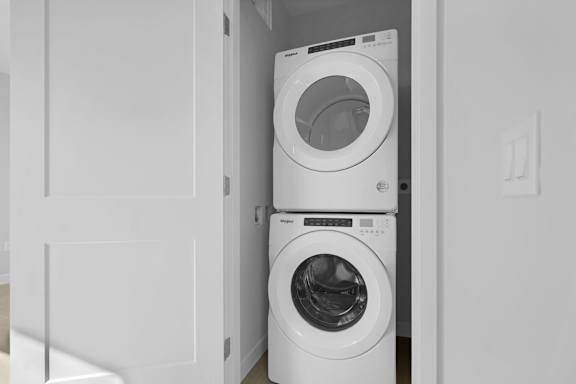 A white washing machine is stacked on top of another white washing machine in a small laundry room.