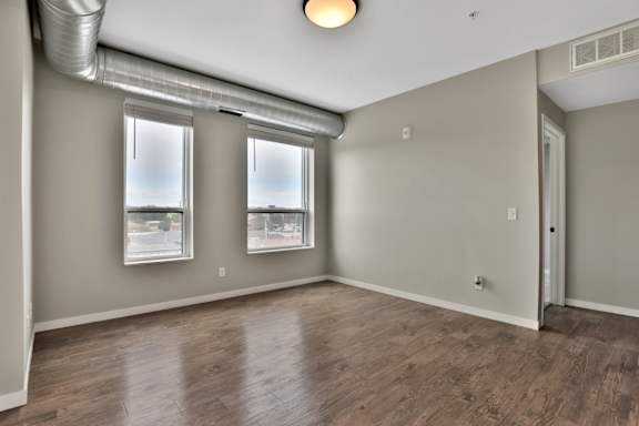 A room with wooden flooring and two windows.