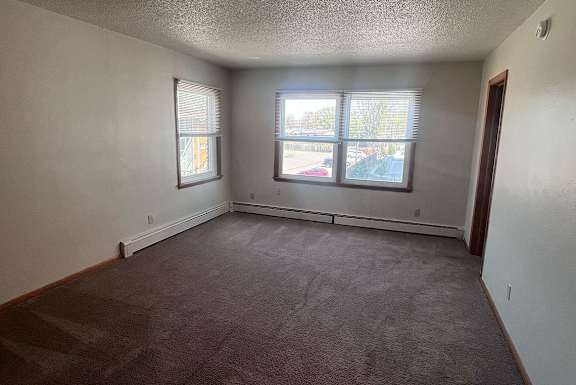 A room with a carpeted floor and two windows.
