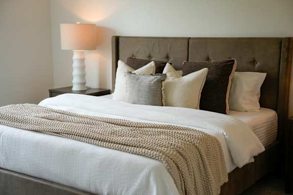 A bed with a white comforter and pillows with a lamp on the side table.