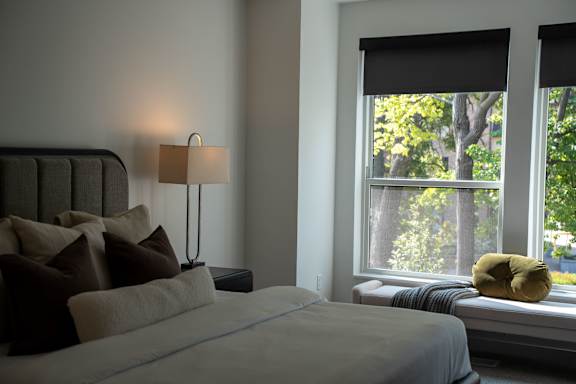A bedroom with a bed, pillows, a lamp, and a window with a view of trees.