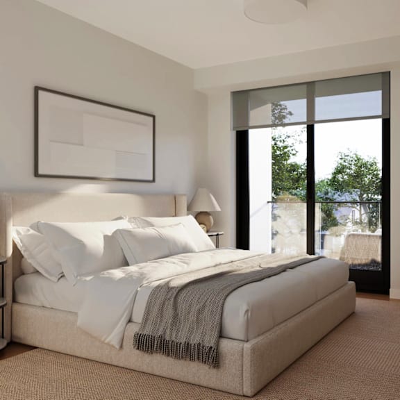 A bed with white pillows and a grey blanket is in a room with a framed picture on the wall.