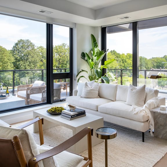 A white couch sits in a living room with a large window behind it.