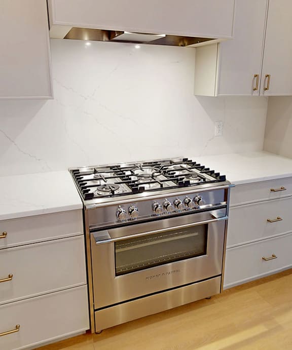 A modern kitchen with a stainless steel gas stove and white cabinets.