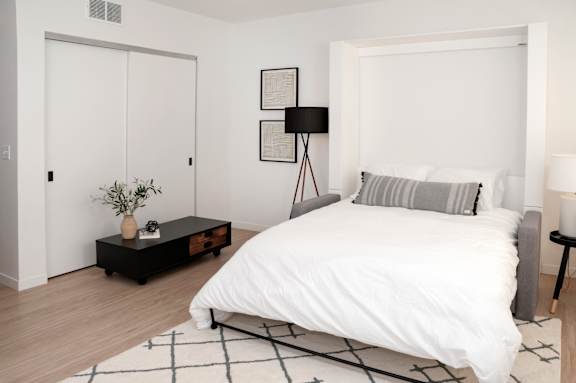 A bedroom with a white bed and a black and white rug.