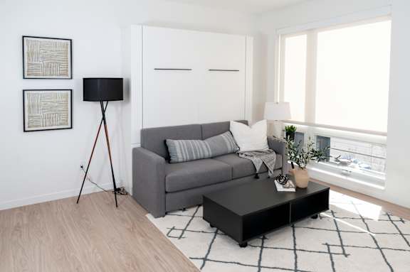 A grey couch sits in a living room with a black floor lamp and a small table with a plant on it.