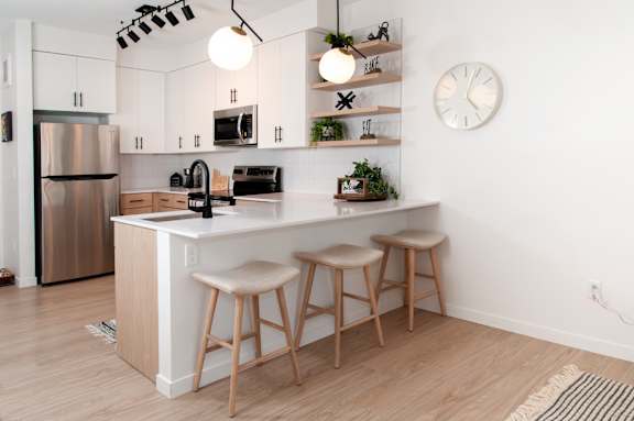 A kitchen with a white refrigerator, a white countertop, and a white wall with a clock.
