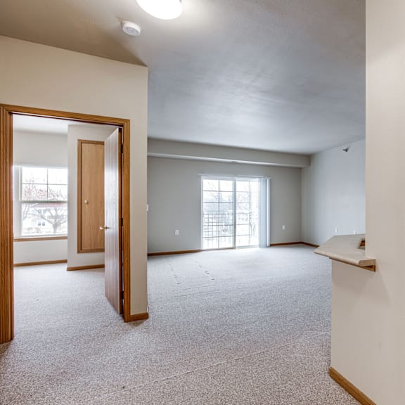 A large, empty room with a carpeted floor and a door leading to a balcony.