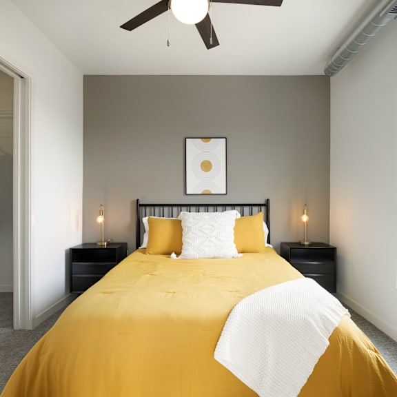 A bed with a yellow comforter and white pillows is in the center of the image.