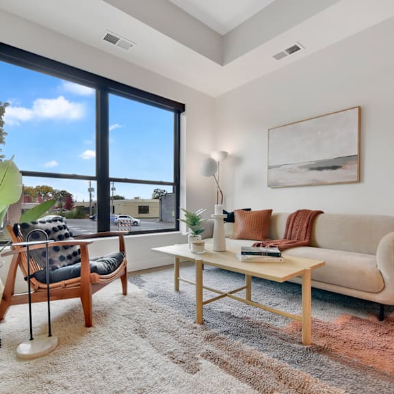 A living room with a large window, a sofa, a chair, a coffee table, and a rug.