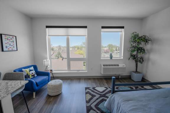 A bedroom with a blue couch and a large window with a view of trees and a building outside.