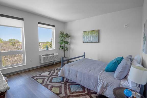 A bedroom with a bed, a plant, and a painting on the wall.