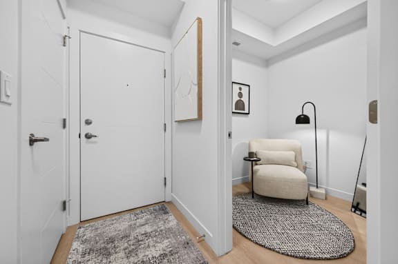 A white door with a silver handle is in a room with a grey rug and a white chair.