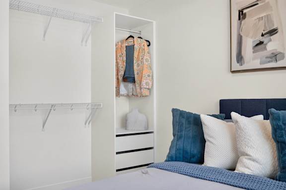 A bedroom with a bed, pillows, a wardrobe, and a painting on the wall.