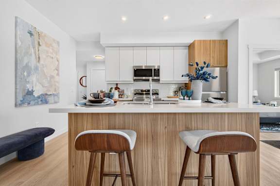 A modern kitchen with a white countertop and wooden bar stools.