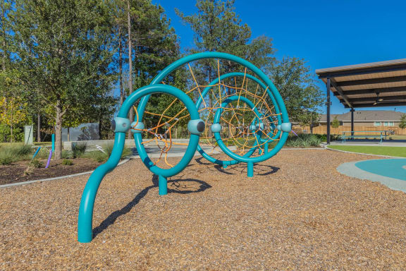a playground with a blue climbing structure and a basketball court in the background at The Village at Granger Pines, Texas