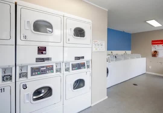 A row of white washing machines are lined up in a laundromat.