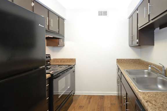 A kitchen with a black fridge, stove and a sink.