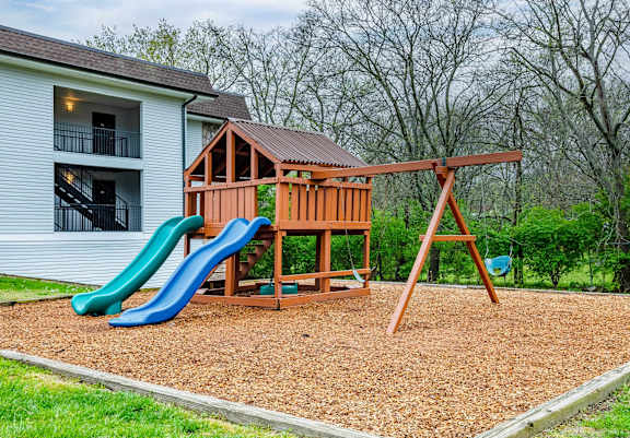 A wooden swing set with a green and blue slide in front of a white house.