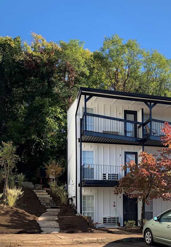 A white house with black railings and a black door is surrounded by trees.