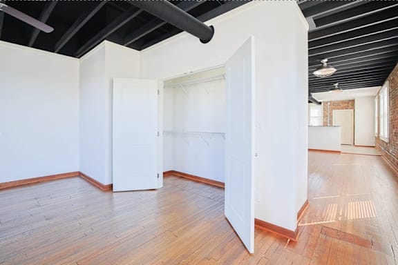 A room with white walls and wooden floors has a white door in the center.