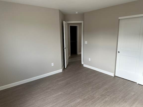 a bedroom and hallway with wood flooring and a door to a closet