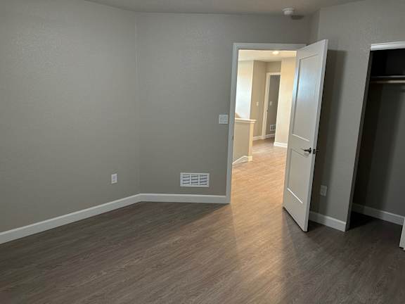 a bedroom and a hallway with wood flooring and a door to a closet