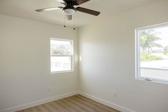 A room with a ceiling fan and two windows.