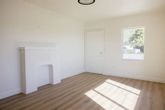 A room with a white door and a window with a view of trees outside.