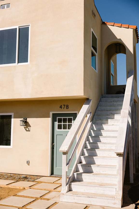 A staircase leads up to a door on a tan building.