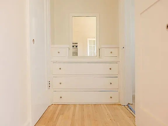 A white dresser with a mirror above it in a room with wooden floors.
