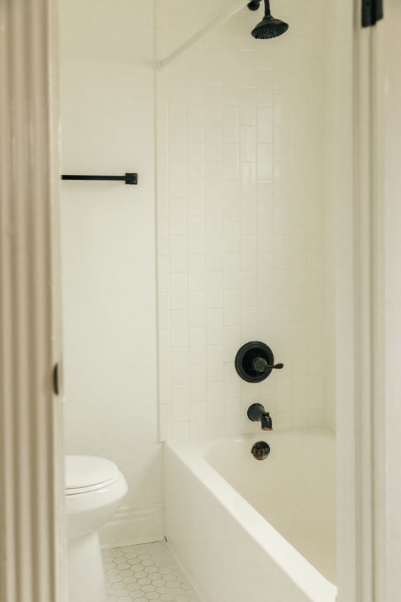 a white bathroom with a white toilet and a white tub with a black shower head