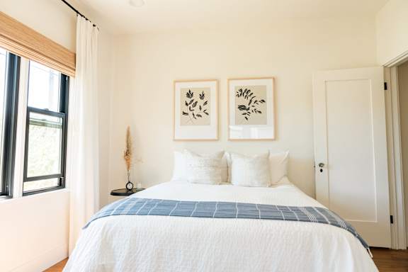 A bedroom with a bed, two pillows, a nightstand, and two framed artworks on the wall.