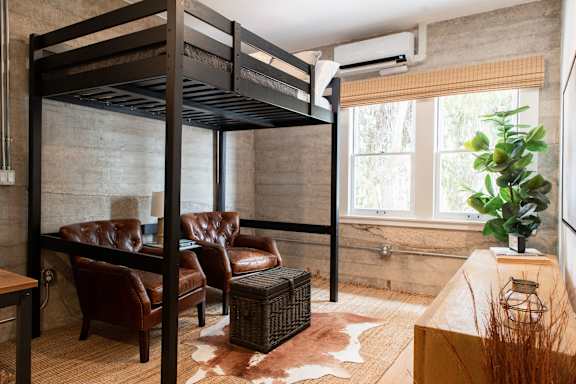 A room with a bunk bed, a chair, a table, and a cowhide rug.