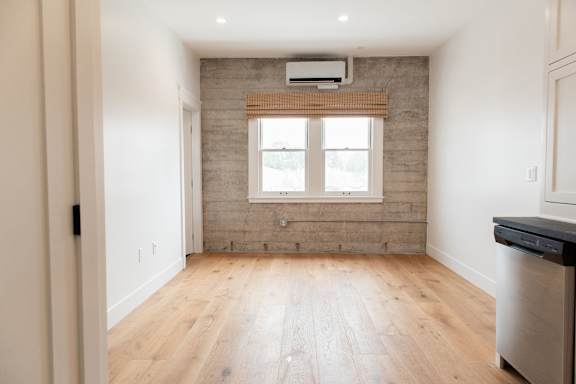 A kitchen with a wooden floor and a window with blinds.