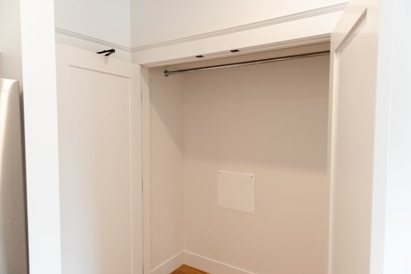 A white closet with a door open and a shelf above it.