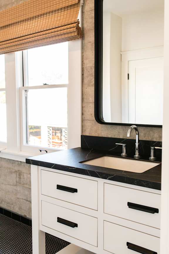 A bathroom with a sink, mirror, and window with blinds.