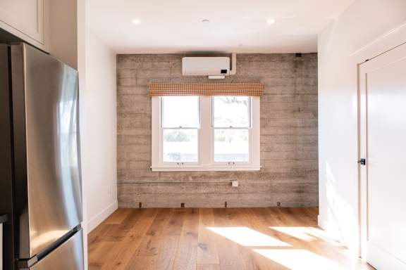 A kitchen with a refrigerator on the left and a window with a white frame on the wall.