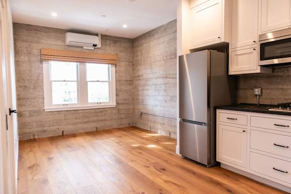 A kitchen with a refrigerator, cabinets, and a window.
