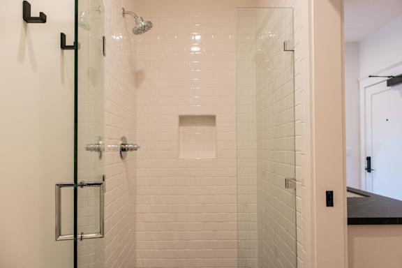 A white tiled shower with a glass door and a black handle.