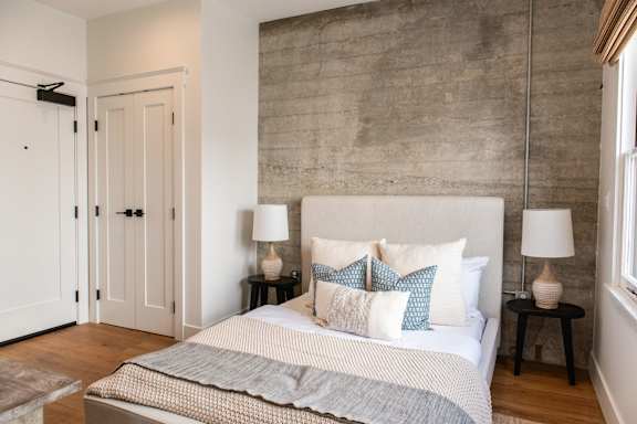 A bedroom with a bed, two lamps, and a brick wall.