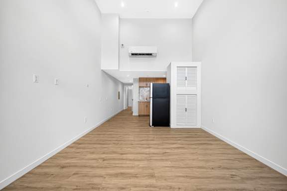 A long hallway with a black fridge and wooden floors.