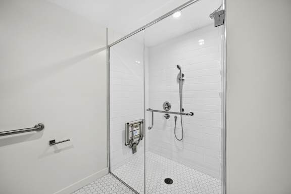 A white tiled shower with a glass door and a shower head.