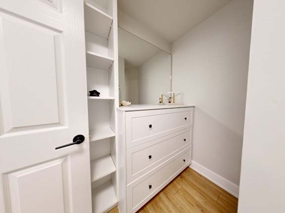 A white door is open to a small room with a dresser and shelves.