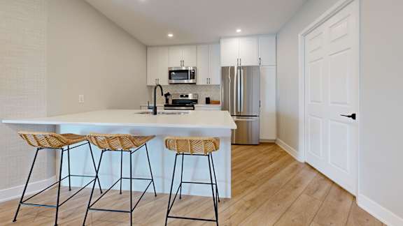 A kitchen with a white countertop and bar stools.
