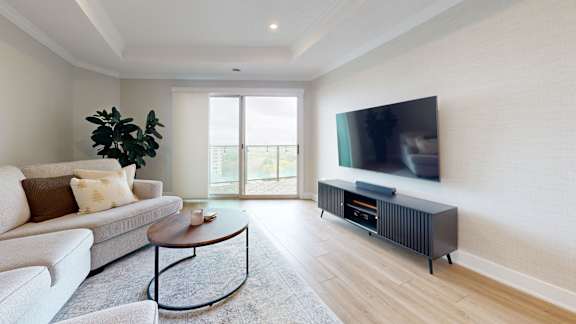 A living room with a white couch, a coffee table, and a flat screen TV mounted on the wall.