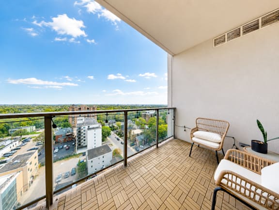 A balcony with a chair and a table overlooking a cityscape.