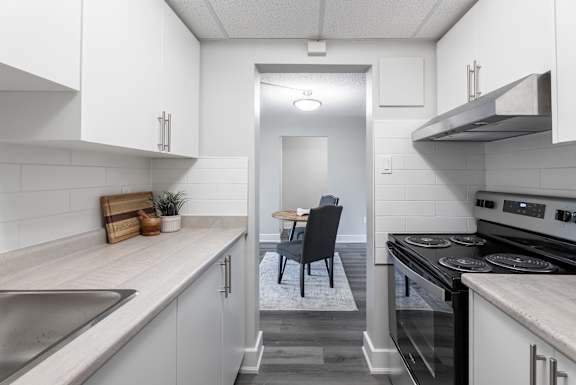 A kitchen with white cabinets and a black chair  at Platts Crossing, London, ON, N6H 4P4