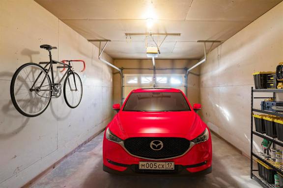 A red car is parked in a garage with a bicycle hanging on the wall.